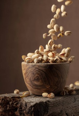 Foto de Flying salted pistachios. Dried nuts in a wooden bowl. Copy space. - Imagen libre de derechos