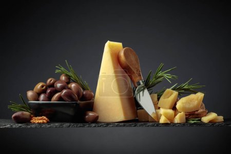 Photo for Parmesan cheese with knife, olives, and rosemary on a black background. - Royalty Free Image