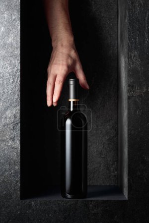 Photo for Hand reach for a bottle of red wine. A concept image on the theme of expensive wines. - Royalty Free Image