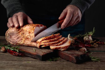 Photo for Hands of a male butcher cutting spicy ham on an old wooden table. Christmas dinner - Royalty Free Image