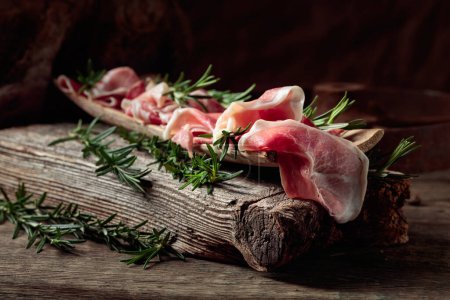 Téléchargez les photos : Crudo de prosciutto italien ou jamon espagnol au romarin sur un vieux fond de bois. - en image libre de droit
