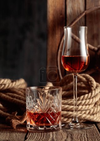 Téléchargez les photos : Verre en cristal et snifter avec rhum, cognac ou whisky sur un vieux fond en bois. Espace de copie. - en image libre de droit