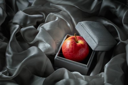 Téléchargez les photos : Une pomme dans une boîte cadeau grise. L'image conceptuelle sur le thème des cadeaux chers. - en image libre de droit