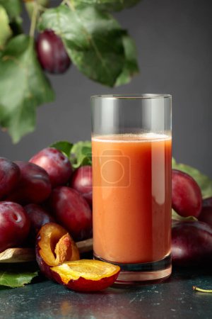 Foto de Vaso de zumo de ciruela sobre una mesa con ciruelas moradas frescas. - Imagen libre de derechos