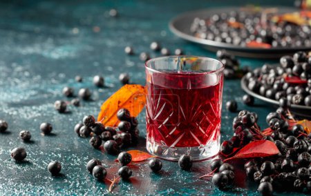 Black chokeberry juice and fresh berries on a dark blue background. Copy space.