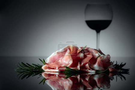 Téléchargez les photos : Prosciutto italien ou jamon espagnol au romarin et vin rouge sur fond noir. - en image libre de droit