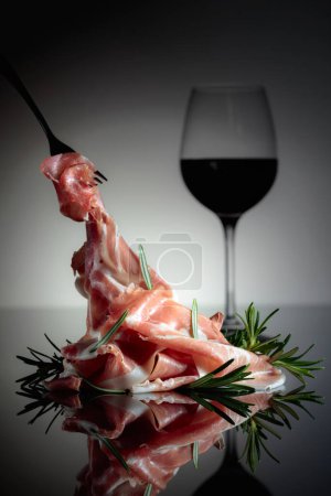 Photo for Italian prosciutto or Spanish jamon with rosemary and red wine on a black background. - Royalty Free Image