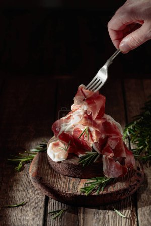 Photo for Italian prosciutto or Spanish jamon with rosemary on an old wooden table. - Royalty Free Image