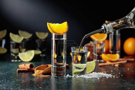 Téléchargez les photos : Tequila is poured into a glass. Tequila with lime and salt, and tequila with orange and cinnamon. - en image libre de droit