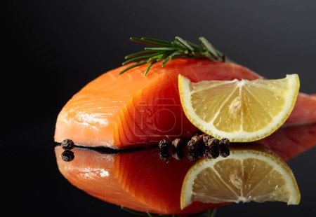Téléchargez les photos : Smocked salmon piece with rosemary, lemon, and peppercorn on a black reflective background. - en image libre de droit