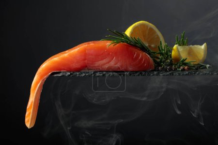 Foto de Smocked salmon with rosemary, lemon, and peppercorn on a black background. Copy space. - Imagen libre de derechos