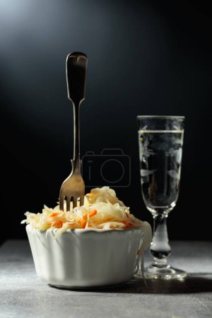 Foto de Bowl of sauerkraut and a glass of vodka on a grey stone table. - Imagen libre de derechos