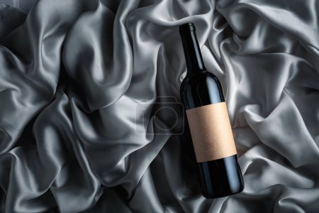 Foto de Bottle of red wine with an empty label on a grey satin background. Top view. - Imagen libre de derechos