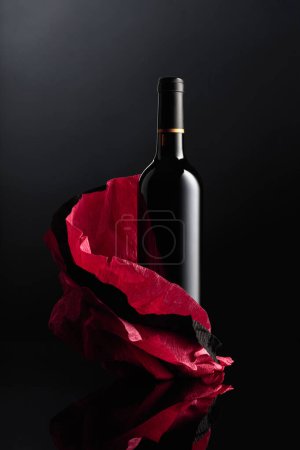 Foto de Botella de vino tinto sobre papel arrugado. Fondo reflectante negro. - Imagen libre de derechos