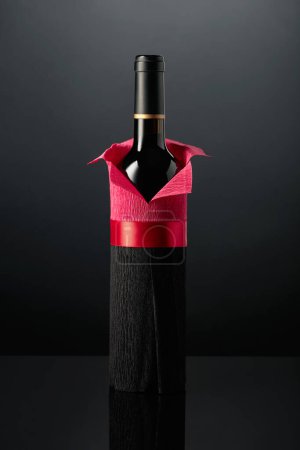 Foto de Botella de vino tinto envuelta en papel crepé sobre fondo negro. La botella parece un hombre con camisa roja.. - Imagen libre de derechos