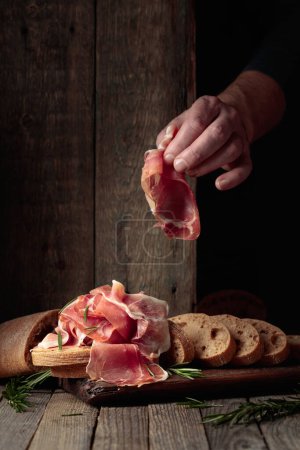 Téléchargez les photos : Prosciutto avec pain et romarin sur une vieille table en bois. Nourriture méditerranéenne traditionnelle. - en image libre de droit
