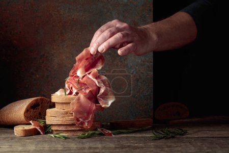 Photo for Prosciutto with bread and rosemary on an old rustic background. Traditional Mediterranean food. Copy space. - Royalty Free Image