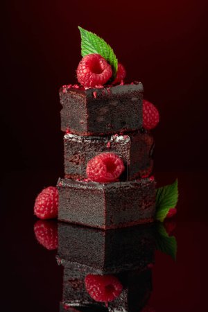 Foto de Pastel de chocolate adornado con frambuesas frescas sobre un fondo rojo oscuro. - Imagen libre de derechos