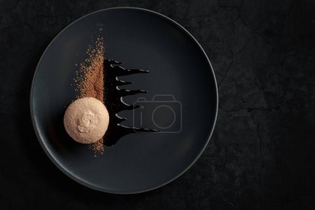 Photo for Macaroon on a black plate garnished with chocolate sauce and cocoa powder. Black stone background with copy space. - Royalty Free Image