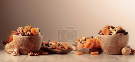 Foto de Dried fruits and nuts on a beige ceramic table. The mix of nuts, apricots, and raisins. Copy space. - Imagen libre de derechos