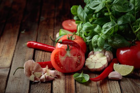 Téléchargez les photos : Ingrédients pour faire de la sauce tomate. Tomates fraîches, poivrons rouges, ail, basilic et citron vert sur une vieille table en bois. - en image libre de droit
