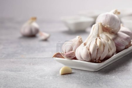 Foto de Garlic in a white dish on a grey stone table. - Imagen libre de derechos