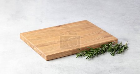 Photo for Cutting board and rosemary on a grey stone table. Culinary background. Empty wooden cutting board, product display space. - Royalty Free Image