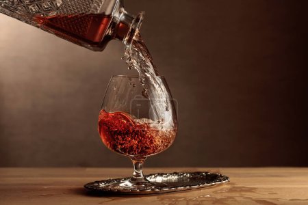 Téléchargez les photos : Le brandy est versé d'une carafe dans un verre de snifter. Cognac sur une table en chêne. Espace de copie. - en image libre de droit
