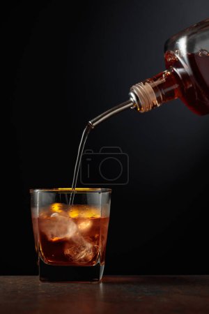 Foto de Whisky se vierte de una botella en un vaso con hielo. - Imagen libre de derechos