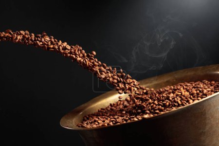 Foto de Medium-roasted coffee beans are poured into an old brass roasting pan. Copy space. - Imagen libre de derechos