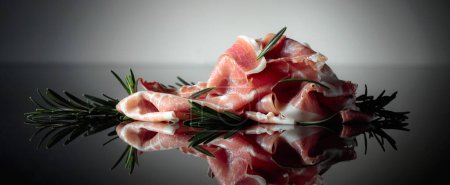 Foto de Italian prosciutto or Spanish jamon with rosemary on a black background. - Imagen libre de derechos
