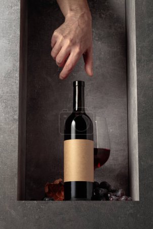 Téléchargez les photos : Vin rouge aux raisins bleus. Sur la bouteille vieille étiquette vide. Main tendue pour une bouteille de vin. - en image libre de droit