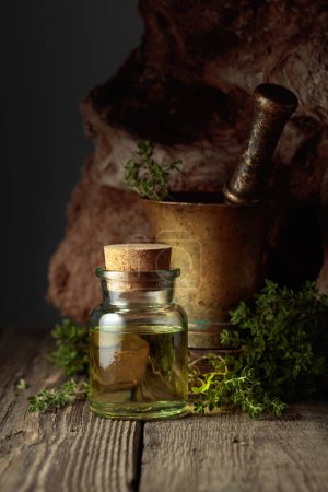 Téléchargez les photos : Bottle of thyme essential oil with fresh thyme twigs on an old wooden table. - en image libre de droit