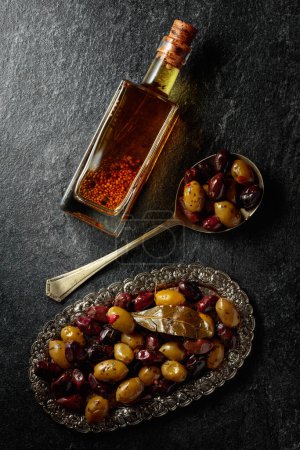Photo for Spicy olives and olive oil on a black stone table. Top view. - Royalty Free Image