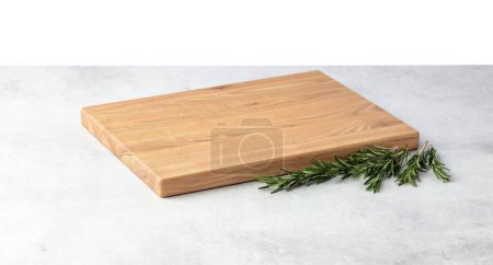 Photo for Cutting board and rosemary on a grey stone table. Isolated on a white background. Culinary background. Empty wooden cutting board, product display space. - Royalty Free Image