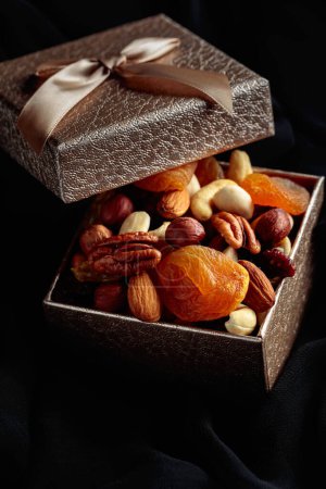 Foto de Frutas secas y frutos secos en una caja de regalo sobre un paño negro. - Imagen libre de derechos