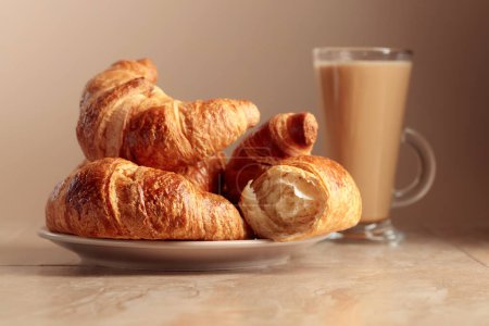Téléchargez les photos : Croissants fraîchement cuits et café à la crème sur une table en céramique beige. - en image libre de droit