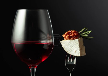 Téléchargez les photos : Verre de vin rouge et fromage Camembert aux noix et romarin sur fond noir. - en image libre de droit
