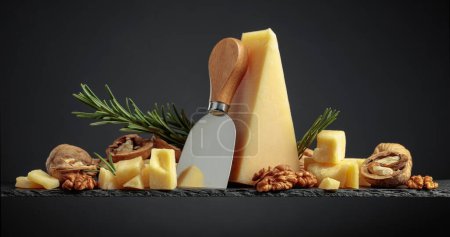 Photo for Parmesan cheese  with knife, rosemary, and walnuts on a black background. - Royalty Free Image