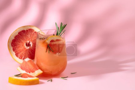 Téléchargez les photos : Cocktail d'été avec pamplemousse, romarin et glace. Boire sur fond rose avec l'ombre de la feuille de palmier. Été, tropical, concept de cocktail frais. - en image libre de droit