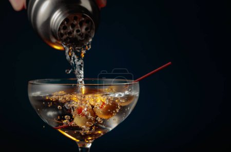 Foto de Martini con aceitunas verdes. El cóctel se vierte de una coctelera en un vaso. - Imagen libre de derechos