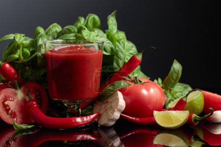 Téléchargez les photos : Sauce tomate épicée avec ingrédients. Tomates fraîches, poivron rouge, ail, basilic et citron vert sur fond noir. - en image libre de droit