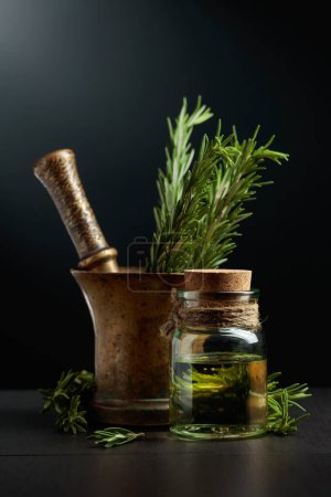 Foto de Botella de extracto de aceite de aromaterapia de romero con ramas de romero fresco y mortero de latón viejo. - Imagen libre de derechos