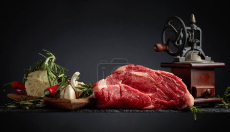 Photo for Raw beef meat steaks with rosemary, garlic, and pepper on a black background. - Royalty Free Image
