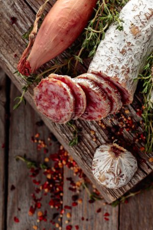 Photo for Traditional dry-cured sausage with thyme, garlic, onion, and spices. Dry-cured sausage on a old wooden table. - Royalty Free Image