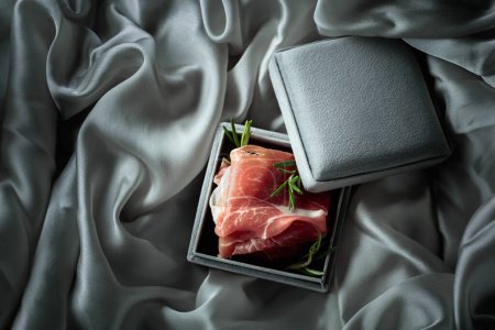 Photo for Prosciutto with rosemary in a gray gift box. Concept of the theme of expensive food. Top view. - Royalty Free Image