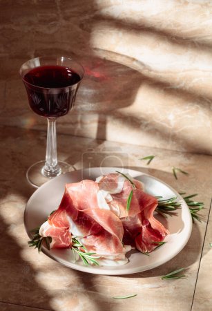 Photo for Italian prosciutto or Spanish jamon with rosemary and red wine on a kitchen table. - Royalty Free Image