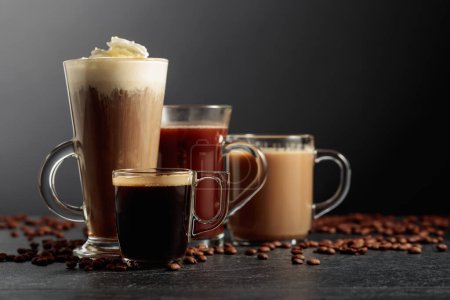 Foto de Varias bebidas de café y chocolate con granos de café dispersos en una mesa negra. - Imagen libre de derechos
