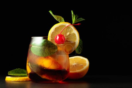 Téléchargez les photos : Cocktail d'été froid et rafraîchissant Cuba libre avec tranches de citron, cerise et menthe sur fond noir. - en image libre de droit