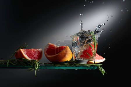Téléchargez les photos : Cocktail gin tonique avec tranches de pamplemousse et brins de romarin. Une tranche de pamplemousse tombe dans le verre créant une belle éclaboussure. - en image libre de droit